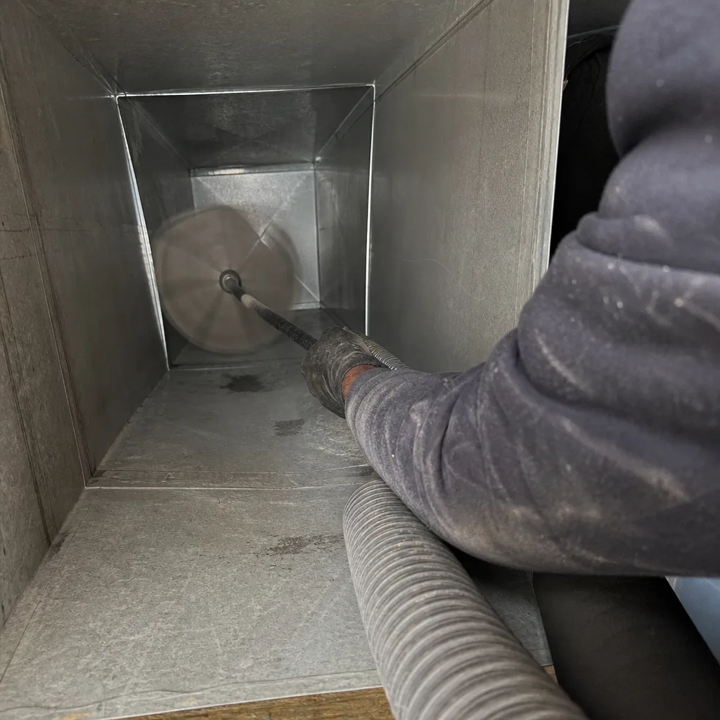 Professional technician performing air duct cleaning with a rotating brush